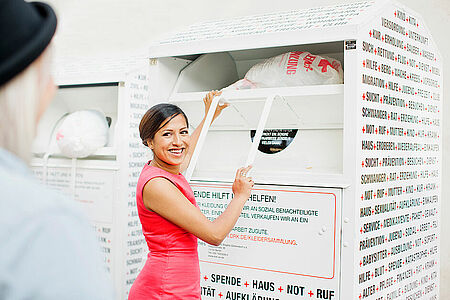 Kleidersammlung des DRK und Altkleidercontainer: junge Frau wirft einen Sack mit Altkleidern in einen Container des DRK